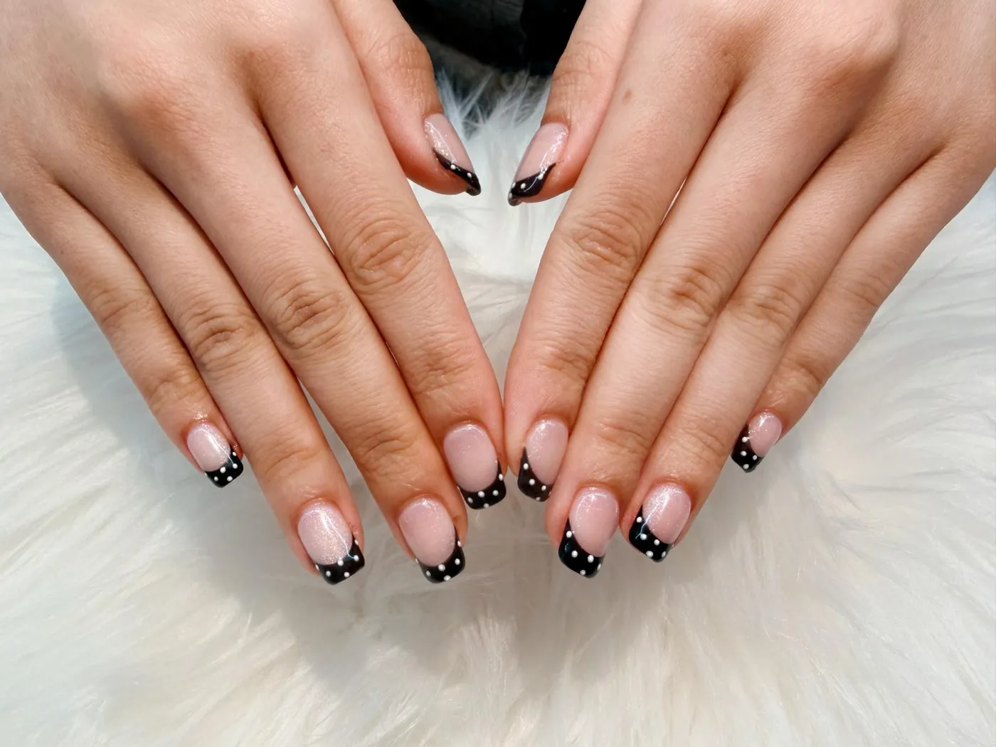 Short nails with black French tips and white polka dots, on white faux fur
