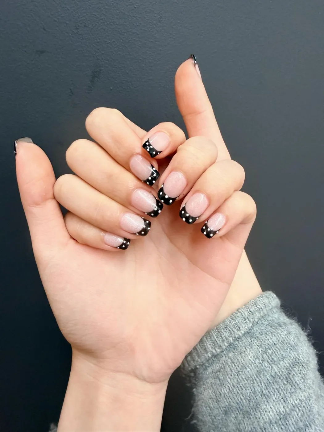 Short natural nails with black polka-dot French tips, a second angle