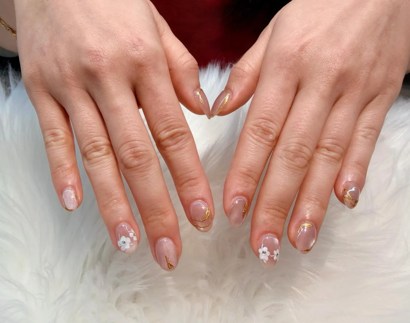 Short nails with tiny white flowers, crystals and gold foil lines on a sheer pink base
