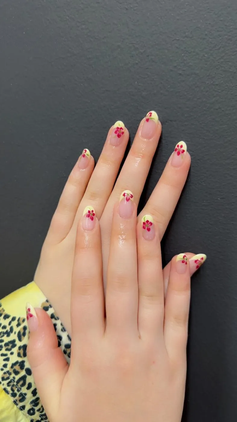 Short natural nails with pale yellow French tips and tiny red flowers