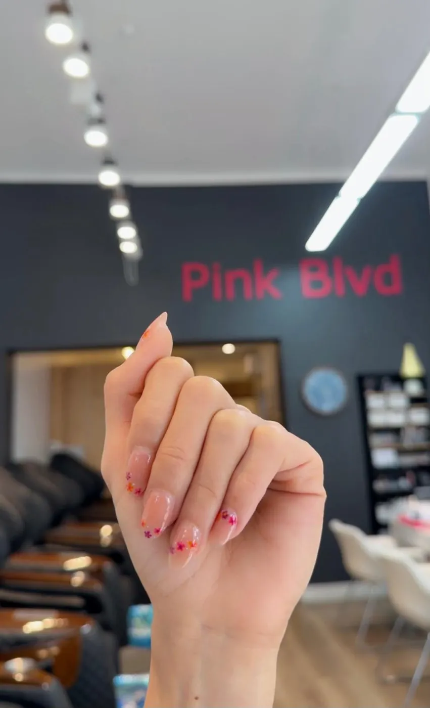 Short nails with tiny flower art held up in front of the Pink Blvd sign inside the Malvern salon