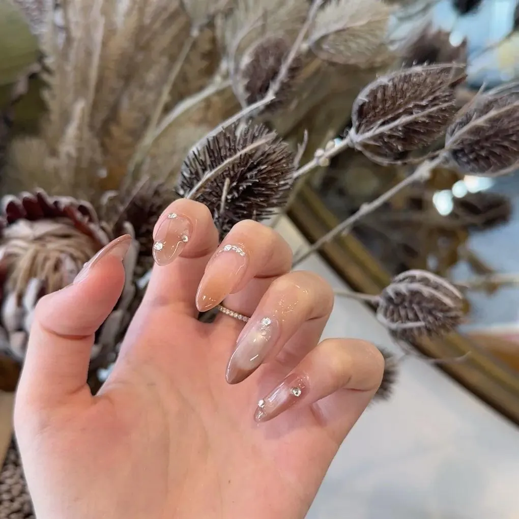Close-up of sheer nude almond nails with chrome shimmer and crystal accents