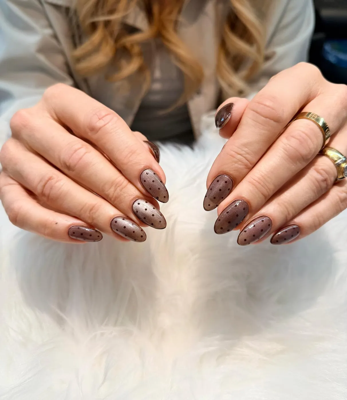 Long almond nails in a sheer smoky plum with fine black polka dots, on white faux fur