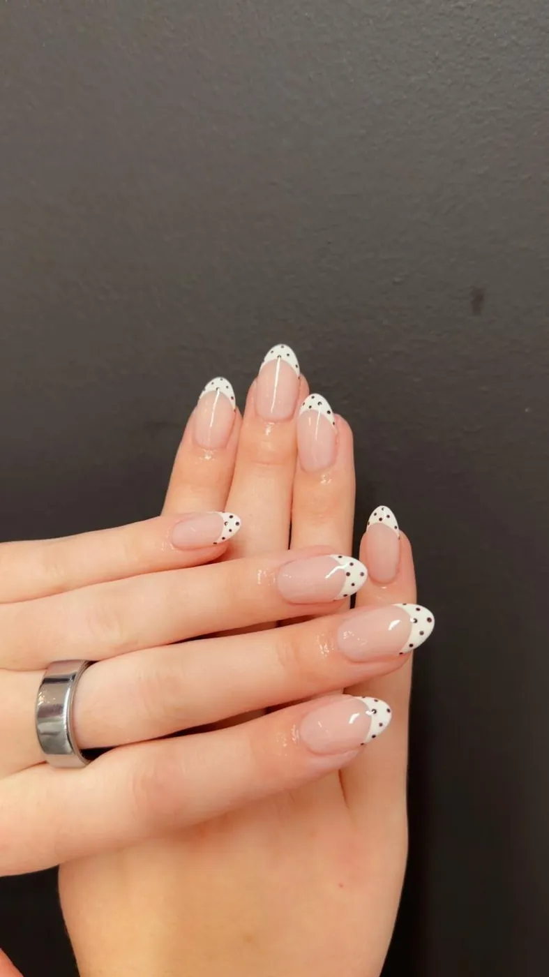 Almond nails in a sheer nude base with white French tips and tiny black polka dots